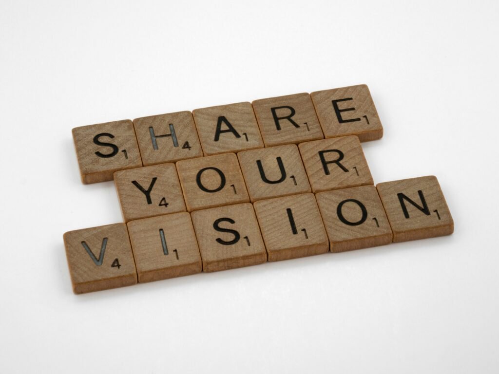 Wooden Scrabble tiles spell out "SHARE YOUR VISION" on a white background.