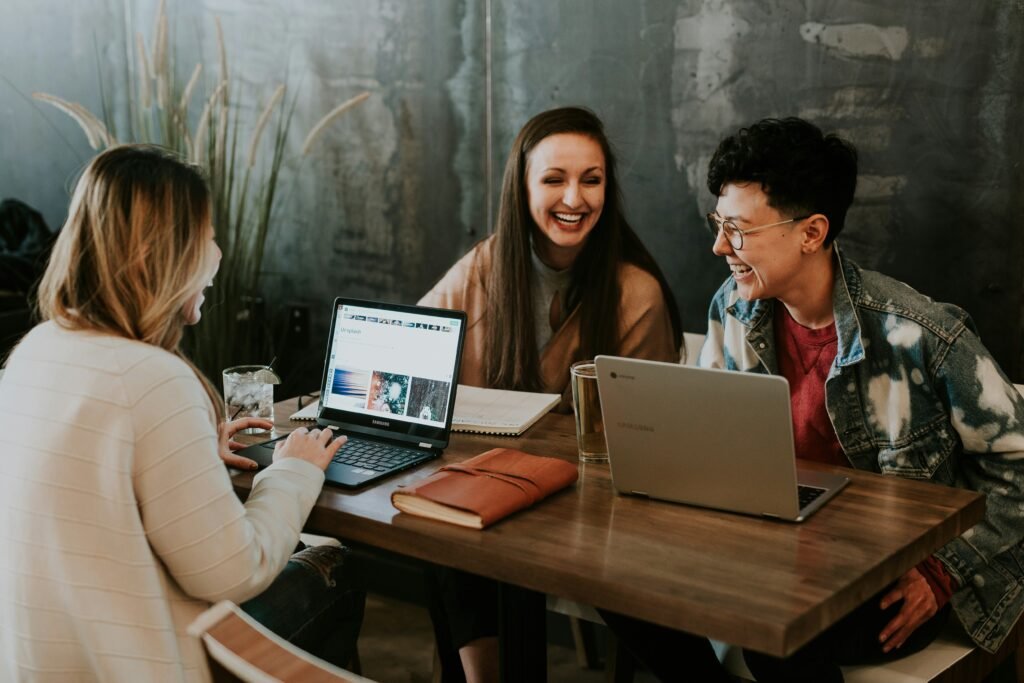 platform how-tos for alt text for images and image seo Three women laugh while working on laptops at a table, as described in the Alt Text Guide for Beginners.