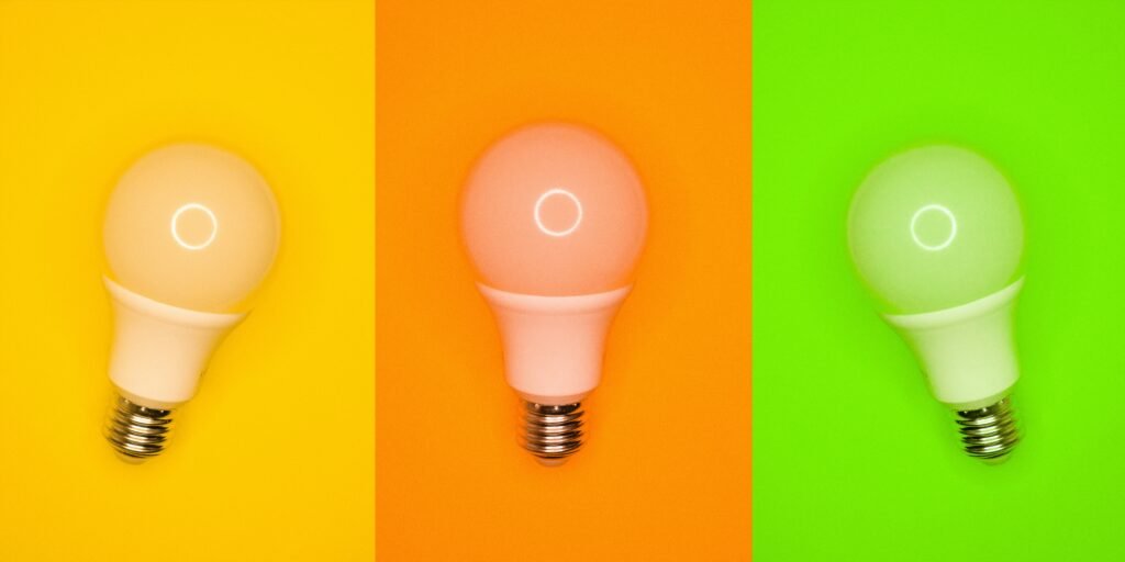 Three light bulbs glow in yellow, orange, and green against matching colored backgrounds.