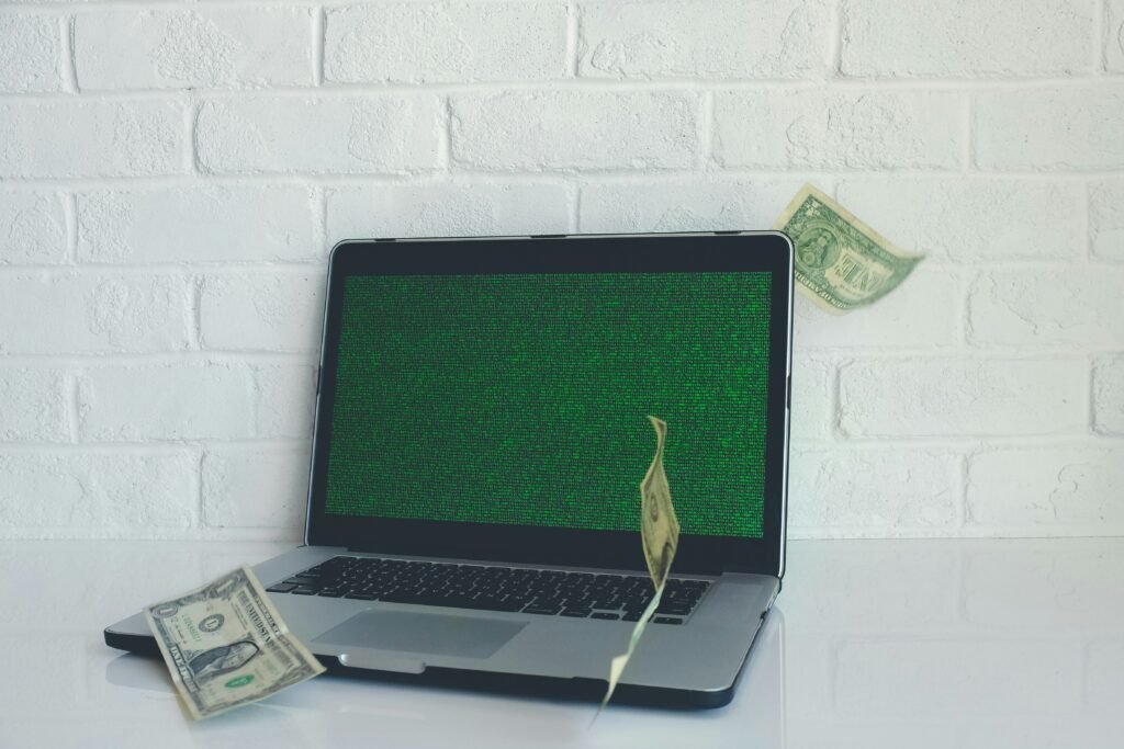 Laptop displaying green code with dollar bills floating around it.