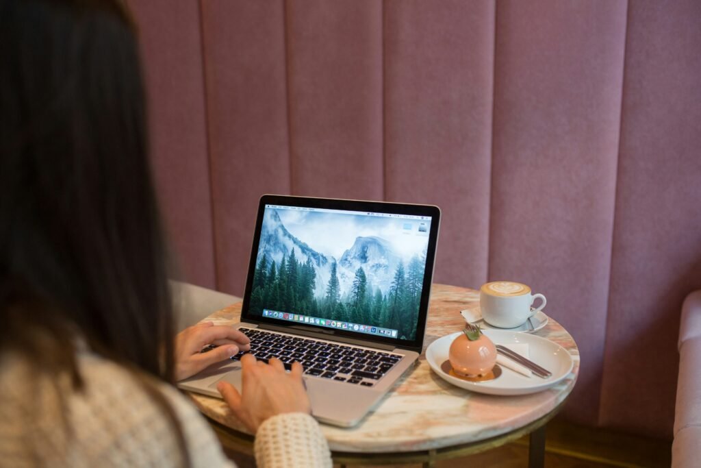 A person types on a laptop with a Yosemite wallpaper, next to a latte and a small cake, as part of a review of the best website tools and products 2025.