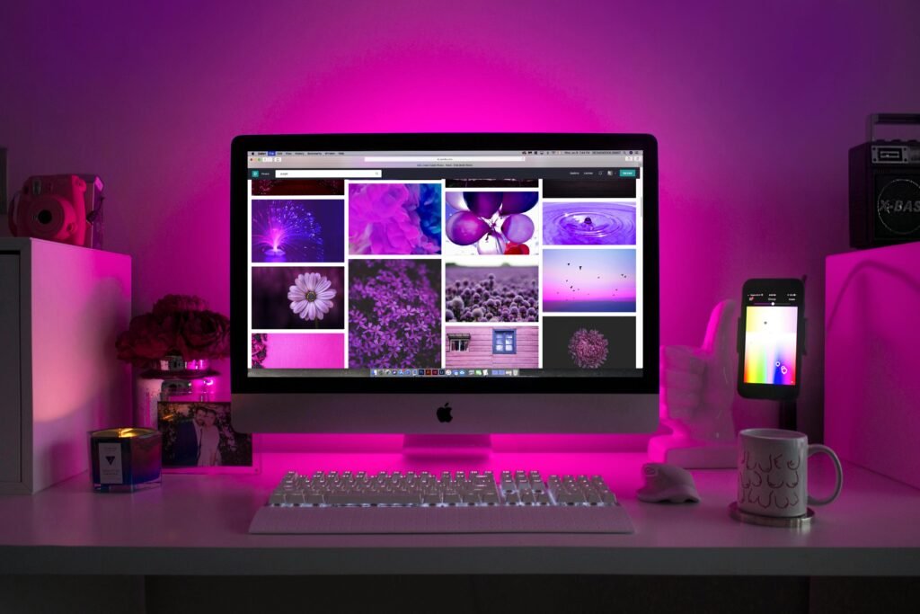 A desk with a computer displaying purple images, a keyboard, a mouse, a candle, and a mug.