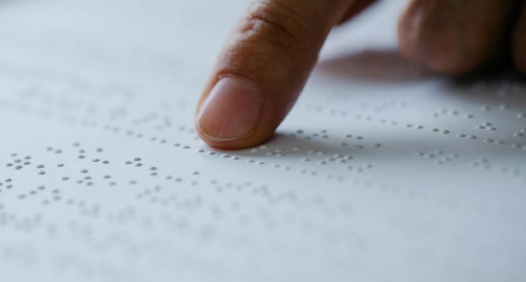A finger reads braille text on a white page.