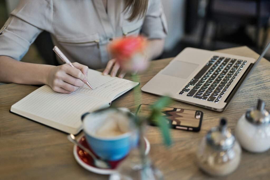 A person writes in a notebook next to a laptop, coffee, and sugar bowls, illustrating SEO Case Studies.