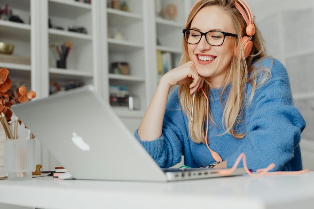 A woman with headphones smiles while looking at her laptop, likely studying SEO Case Studies.