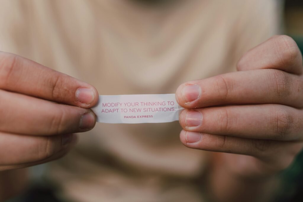Hands hold a fortune cookie slip with the message "MODIFY YOUR THINKING TO ADAPT TO NEW SITUATIONS. PANDA EXPRESS.".