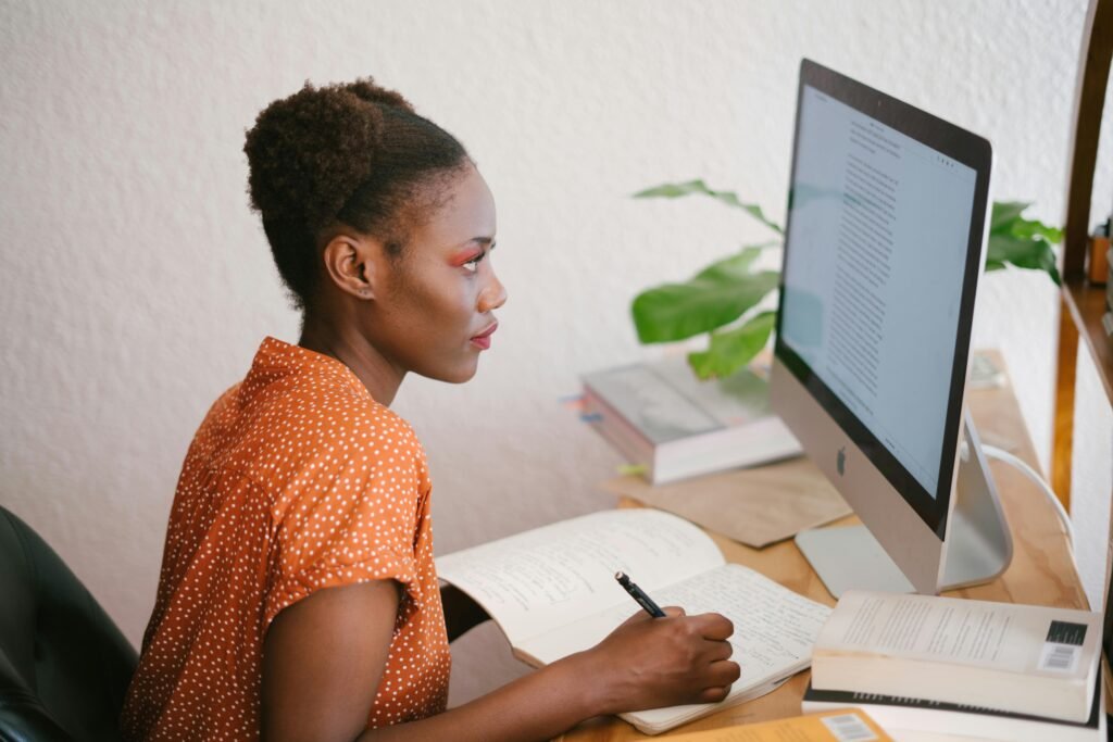A woman in an orange polka-dot shirt writes in a notebook while looking at a computer screen displaying SEO Case Studies.