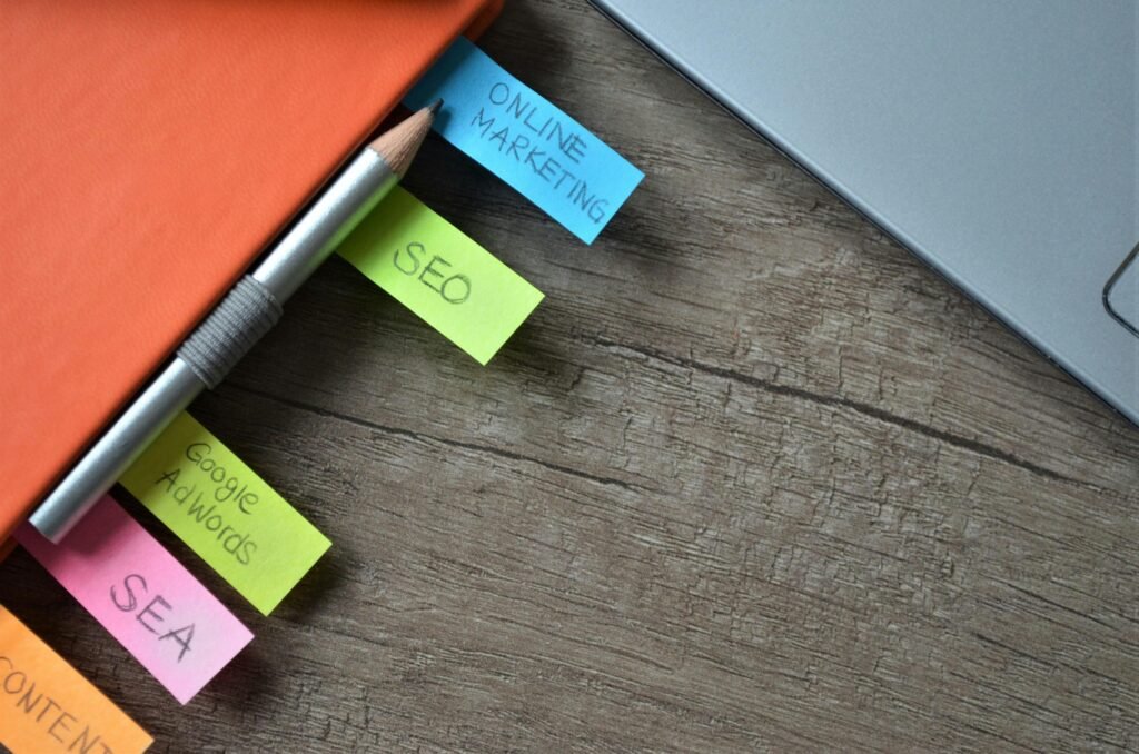 A pencil rests on a notebook with sticky notes labeled "Online Marketing," "SEO," "Google AdWords," and "SEA," suggesting a focus on the best website tools and products 2025.