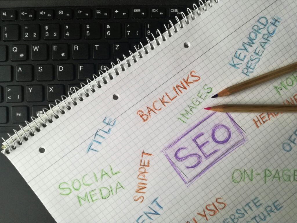 Notebook page with SEO terms like "keyword research" and "social media" written on it, next to a laptop keyboard.