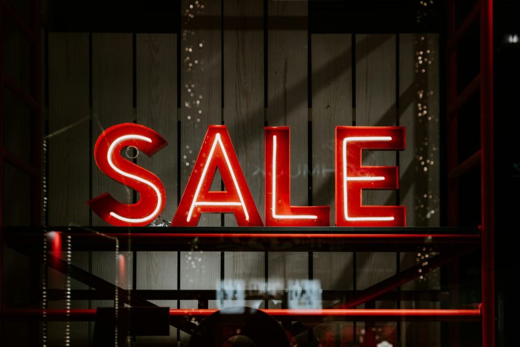 Red neon letters spell out "SALE" in a store window.