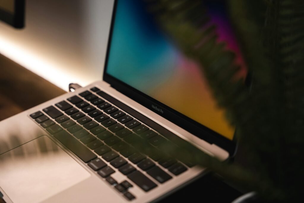 A MacBook Pro displays a colorful gradient wallpaper, with a plant partially obscuring the screen.