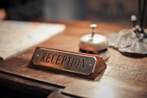 A metal "RECEPTION" sign sits on a wooden desk next to a silver bell