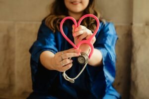 Nurse holds pink stethoscope in a heart shape with a blurred background