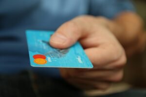 Hand holding a blue debit card with Mastercard and Paypass logos