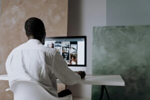 Man in white shirt works on a computer displaying a grid of images