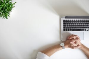 Hands clasped on a laptop keyboard next to a potted plant