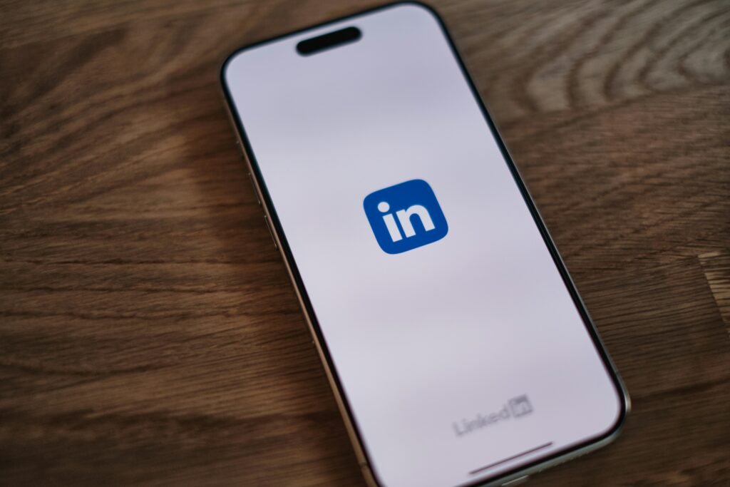 Smartphone screen displays the LinkedIn logo and text on a wooden surface