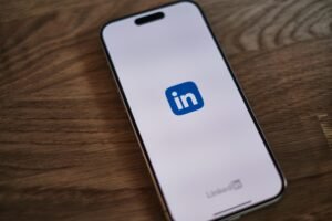Smartphone screen displays the LinkedIn logo and text on a wooden surface
