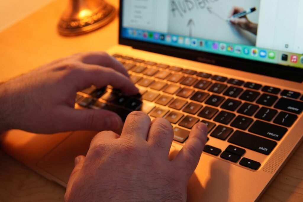 Hands typing on a laptop keyboard with a warm orange glow