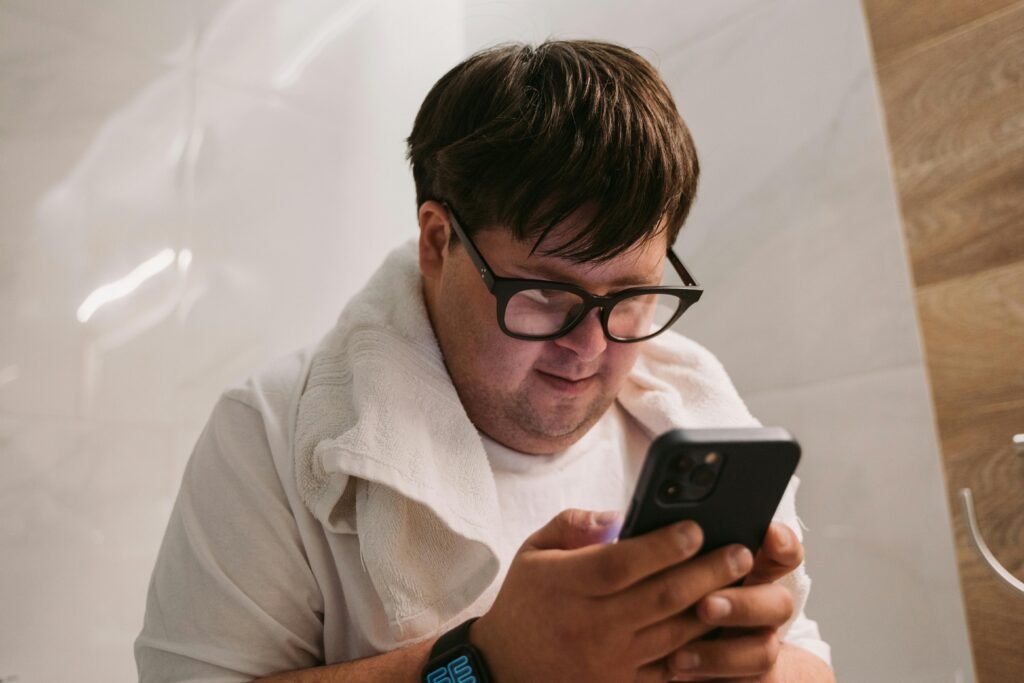 A man wearing glasses and a towel around his neck looks at his smartphone, demonstrating ai accessibility