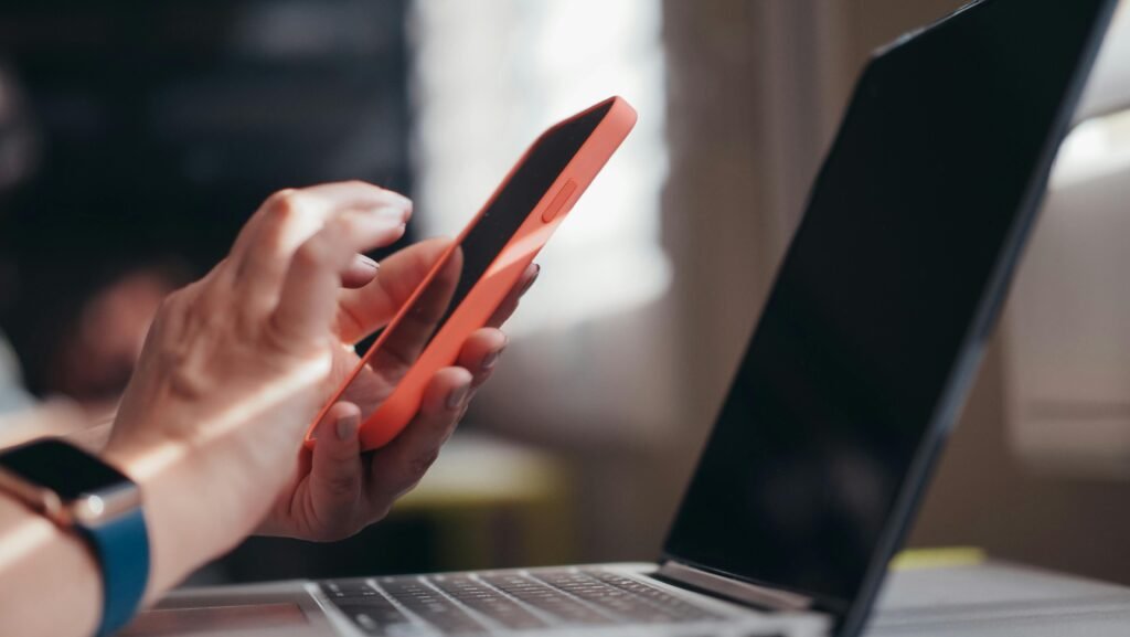 A person's hands hold an orange smartphone next to a laptop, demonstrating ai accessibility