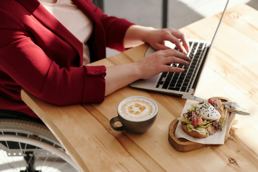 A person in a wheelchair works on a laptop at a wooden table with a latte and an open-faced sandwich, illustrating the importance of ADA compliant websites