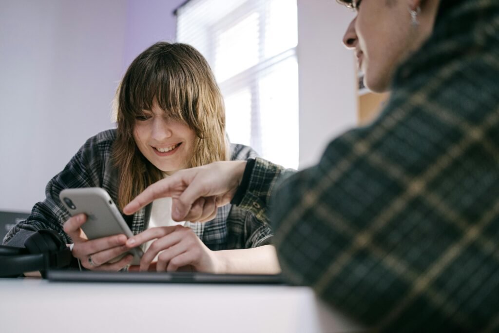A woman smiles as she points at a smartphone held by her friend, discussing accessbility laws 2026