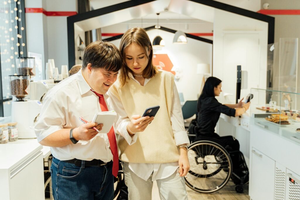 A man with Down syndrome and a woman look at a phone while a woman in a wheelchair works behind a counter
