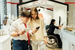 A man with Down syndrome and a woman look at a phone while a woman in a wheelchair works behind a counter