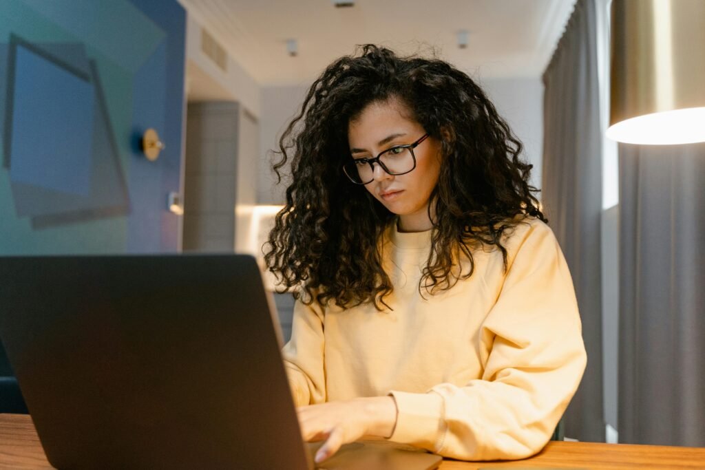 A woman with curly hair and glasses works on a laptop, possibly engaged in ai model training