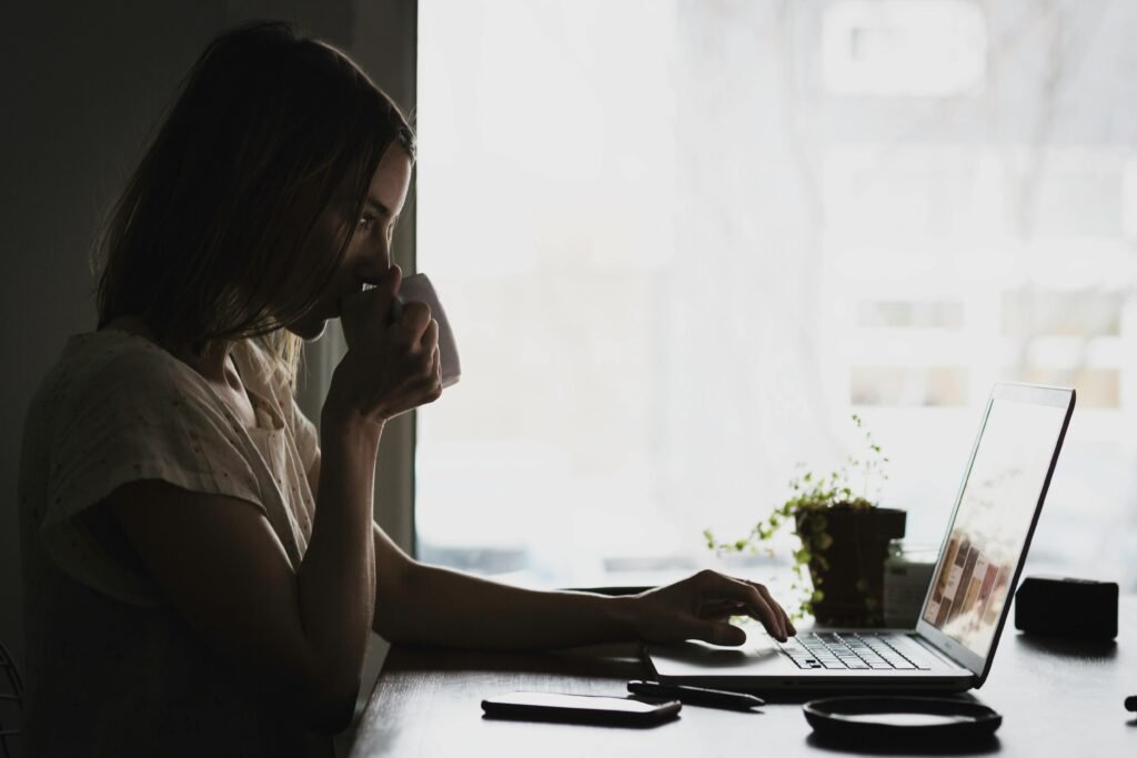 A woman drinks from a mug while working on a laptop, surrounded by the image compression tools of a digital nomad