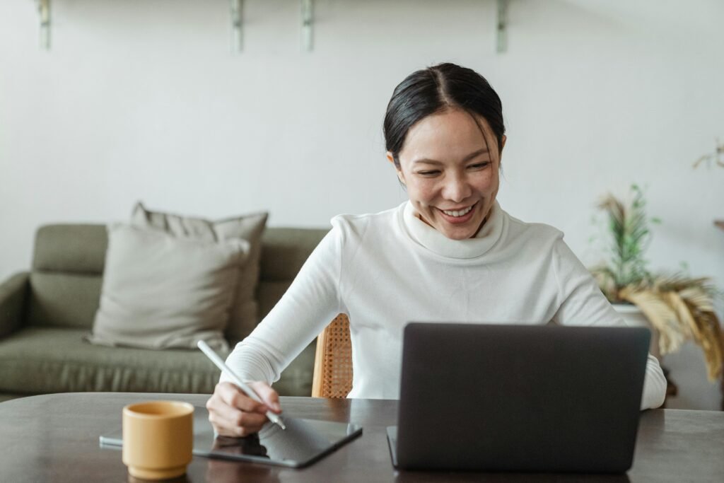 Woman smiles while working on a laptop and tablet at a table