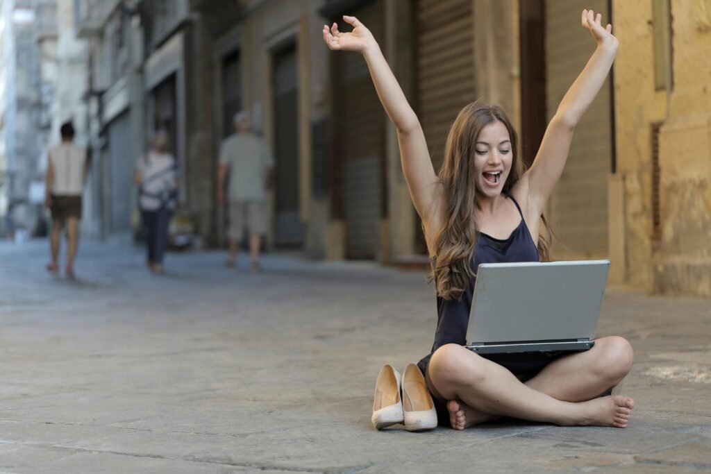 Woman with arms raised in celebration while using a laptop on a city street