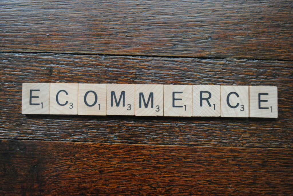 Wooden Scrabble tiles spell out "E COMMERCE" on a dark wood surface