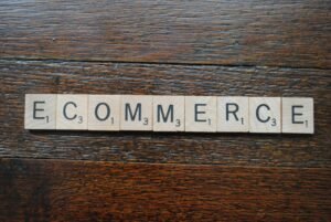 Wooden Scrabble tiles spell out "E COMMERCE" on a dark wood surface