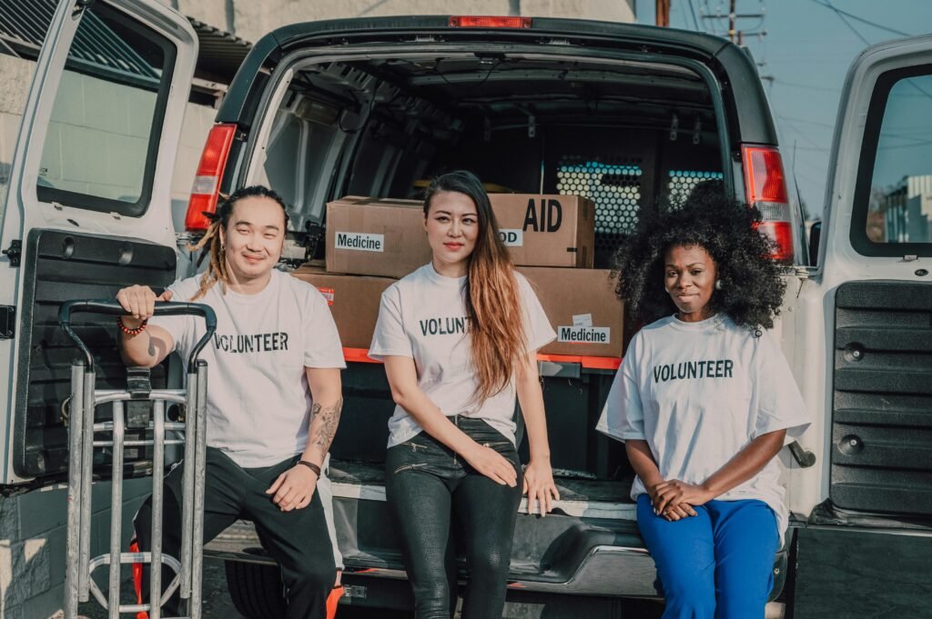 Three volunteers in white t-shirts sit in the back of a van filled with boxes of aid and medicine