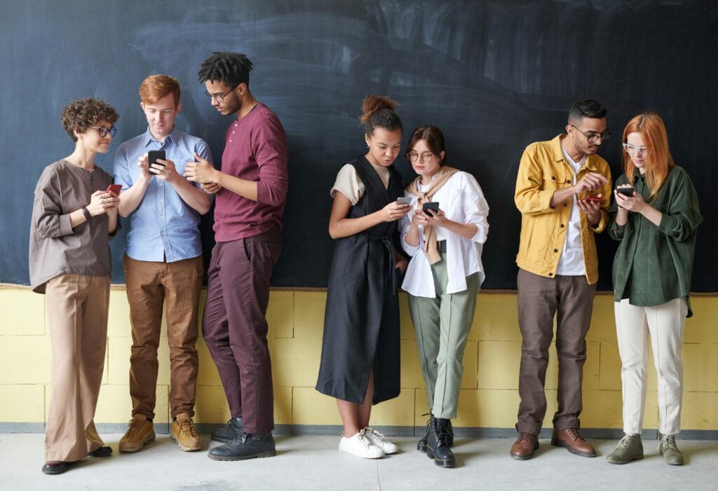 Six young adults stand in front of a blackboard, each engrossed in their smartphones, illustrating the importance of good alt text for screen readers