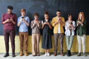 Seven young adults stand in a line, each engrossed in their smartphones, illustrating the need for good alt text for screen readers