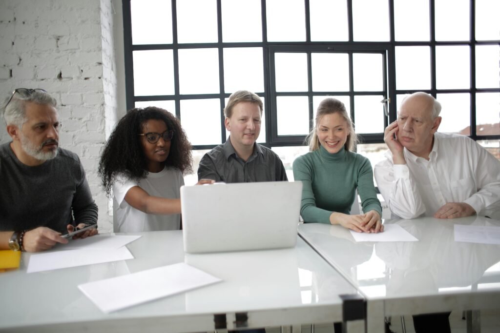 A diverse group of five people sit at a table, looking at a laptop, as they learn how to fix image alt text