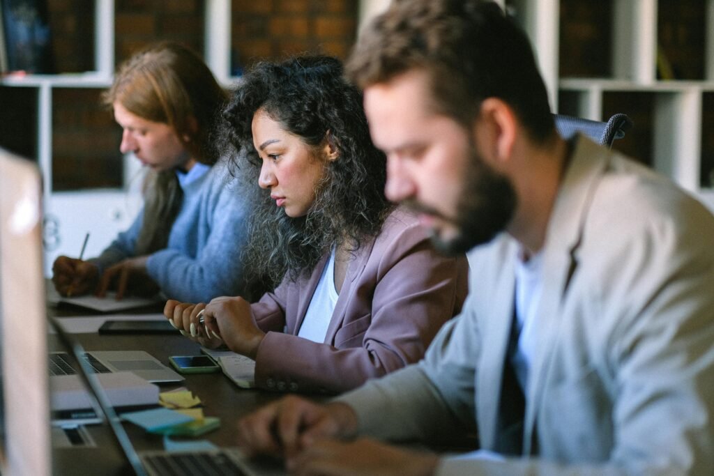Three people work at laptops, with one woman focused on her screen, possibly using a Chrome AI alt text generator