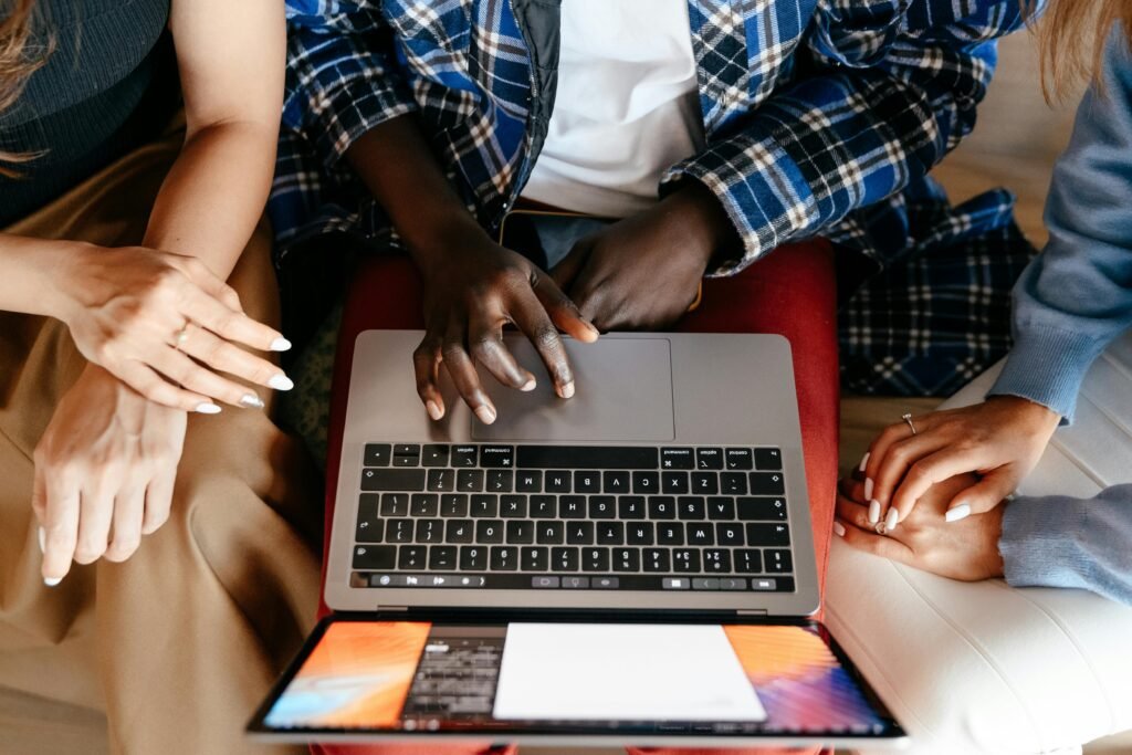 Three people's hands are visible around a laptop, with one person's fingers on the keyboard, suggesting they are using a Chrome AI alt text generator