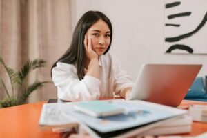 Young woman with hand on cheek looks at a laptop on an orange desk