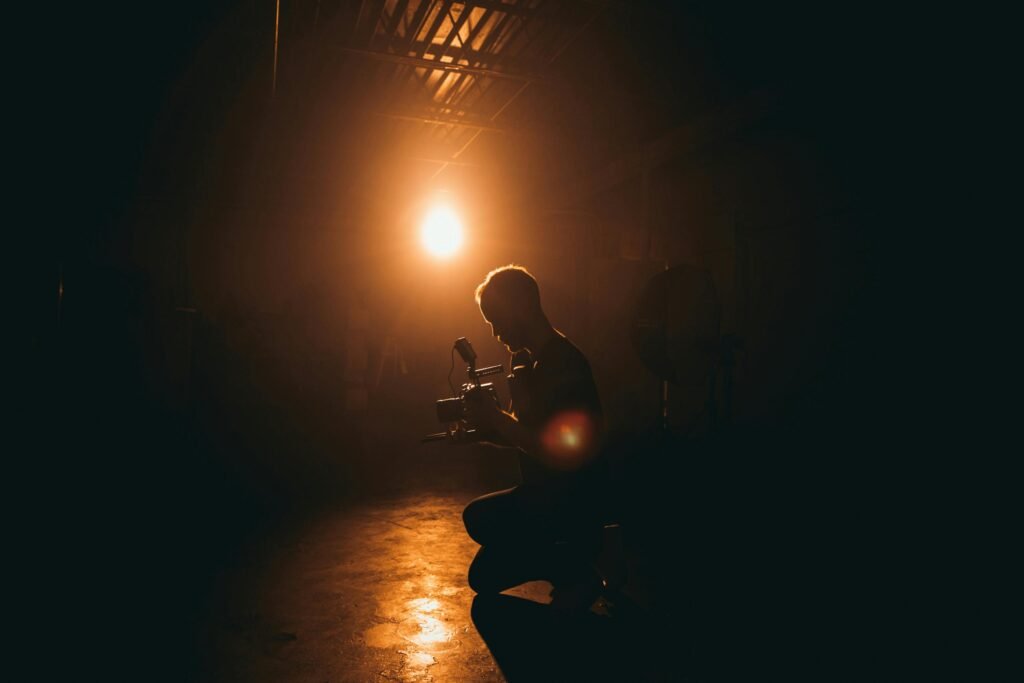 A silhouette of a photographer kneels with a camera rig, illuminated by a bright orange light