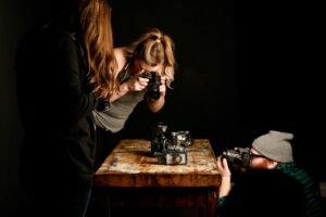 Three people focus on cameras on a wooden table, hinting at the importance of photography seo