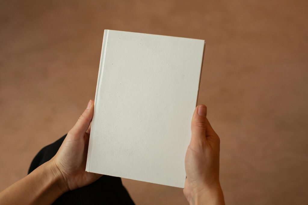 Hands hold a blank white book against a brown background