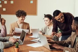 Colleagues collaborate around a wooden table with laptops and papers