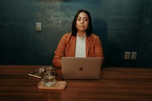 A woman sits at a wooden desk with a laptop, a glass of water, and a notebook, working on wordpress accessibility tools