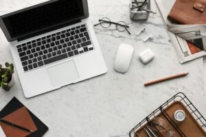 A laptop, mouse, earbuds, and glasses are arranged on a marble desk, illustrating how core web vitals images impact SEO success