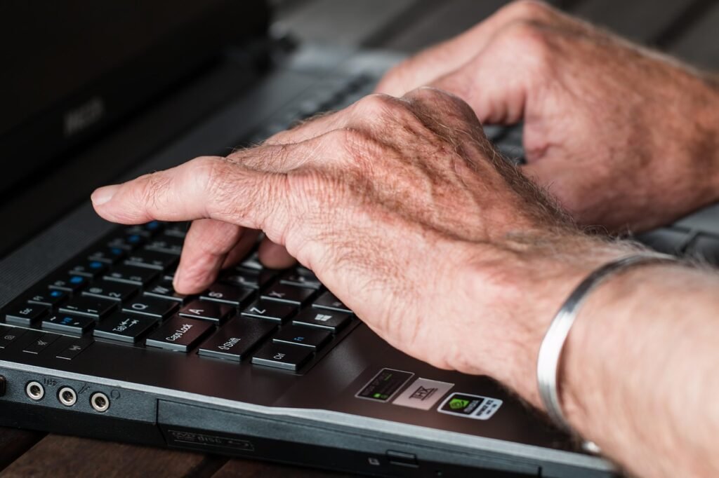 An older person's hands type on a laptop keyboard, suggesting large image library processing
