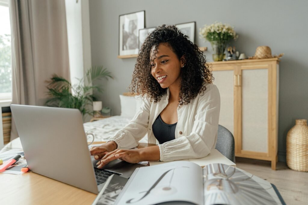 A woman with curly hair smiles as she types on a laptop, with an open magazine and highlighters on the desk, demonstrating ethical ai in action